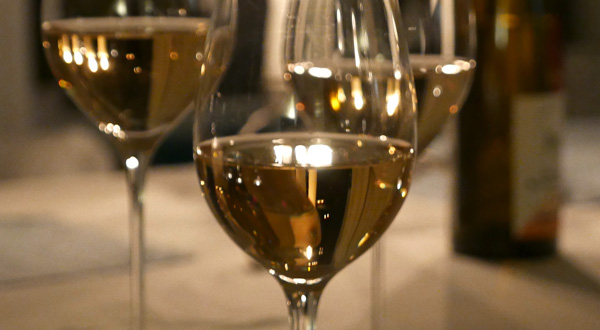 Tre glas med vitt vin med tända ljus i bakgrunden