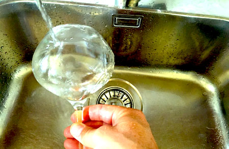 ett vinglas som diskas under rinnande vatten
